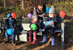 Bild vergr&ouml;&szlig;ern: Die Kindergartenkinder des AWO-Familienzentrums nehmen sofort Platz auf der neuen Bildungsinsel in Hadem. Auf dem Bild steht Tomas Irle hinter der Bank, auf der drei Kinder sitzen. Ein M&auml;dchen liest ein Buch.