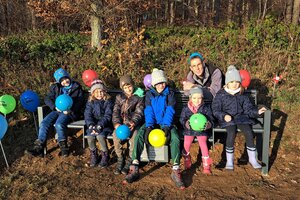 Bild vergr&ouml;&szlig;ern: Die Kinder, die an diesem Tag zur Bildungsinsel in Hadem gekommen sind, nehmen zum ersten Mal auf der neuen Lesebank Platz. Hinter ihnen hockt Tomas Irle, Initiator des Projekts.
