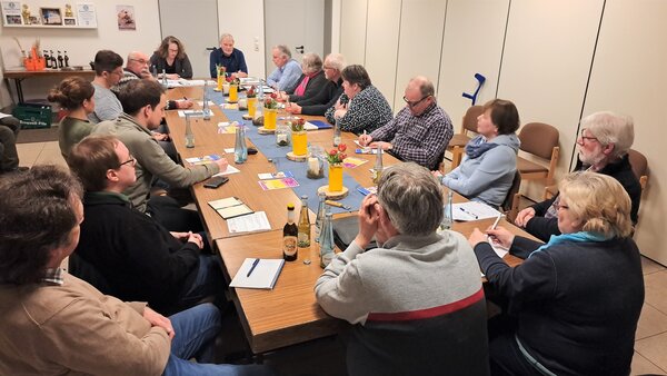 In der Kapellenschule in Helberhausen kommen die Vertreter der Heimatvereine und die Ortsheimatpfleger ins Gespr&auml;ch. Das Bild zeigt die M&auml;nner und Frauen im Austausch. Sie sitzen an einem langen Tisch im kleinen Raum der Kapellenschule. 