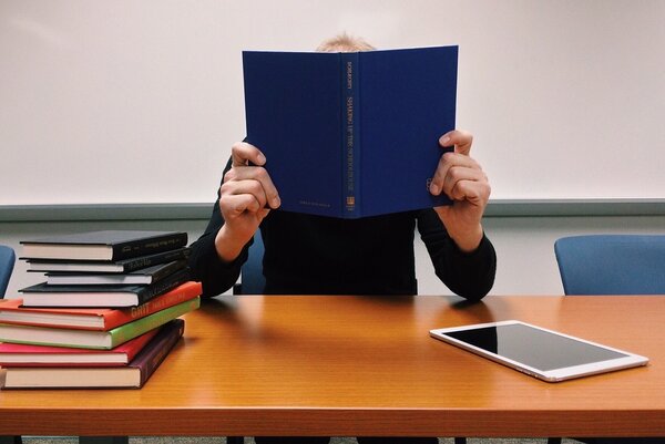 Das Bild zeigt eine Person, die ein Buch liest. Neben ihr liegen weitere B&uuml;cher und ein Tablet.