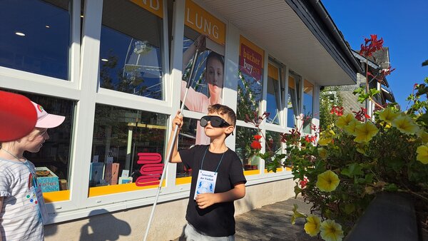 Interessierter Junge mit Brille und Blindenstock gewinnt erste Eindr&uuml;cke dar&uuml;ber, wie es ist blind zu sein.